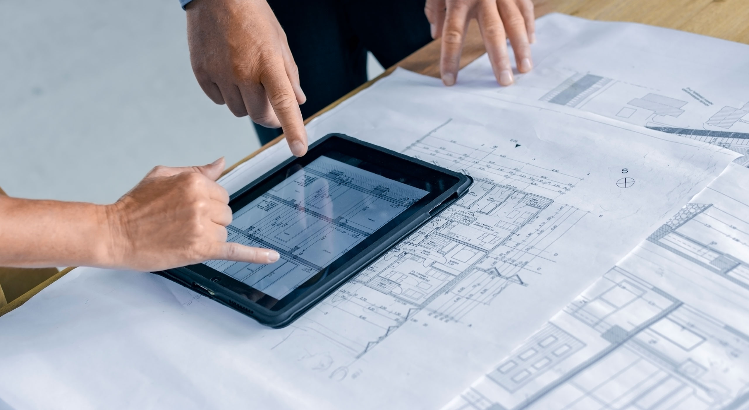 Hands pointing at a tablet displaying blueprints during facility planning and condition assessment services.